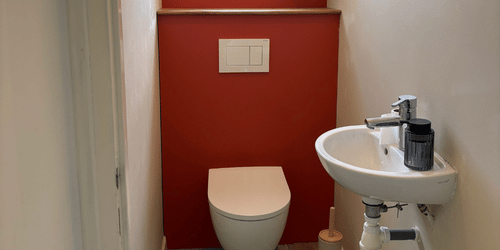 WC suspendu et lave-mains dans des toilettes avec un mur rouge